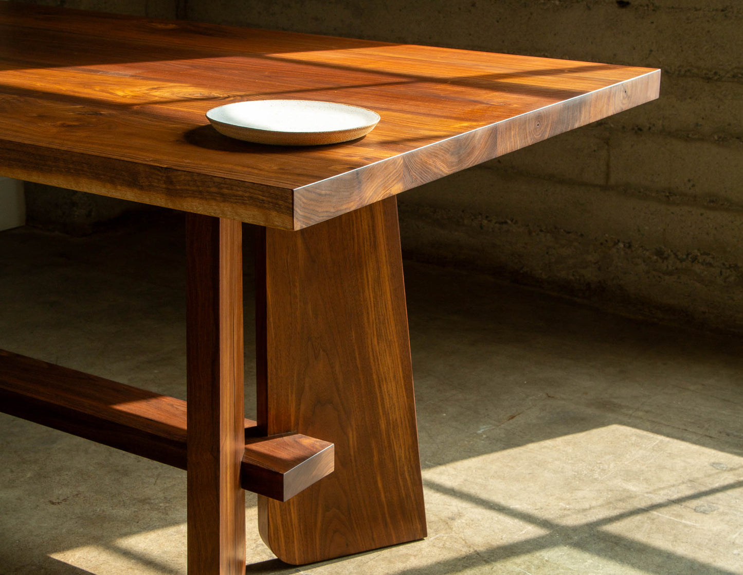 A close-up detail shot of a hand-built Snyder DePass Temple dining table, showcasing the precise joinery and beautiful grain of the solid Walnut wood.