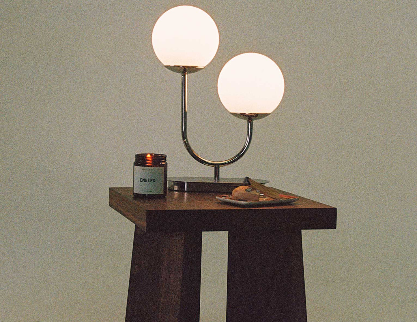 A warm, film-style photograph of the hand-built Snyder DePass Temple Stool, here being used as a side table, highlighting its solid Walnut construction and clean, sculptural silhouette.