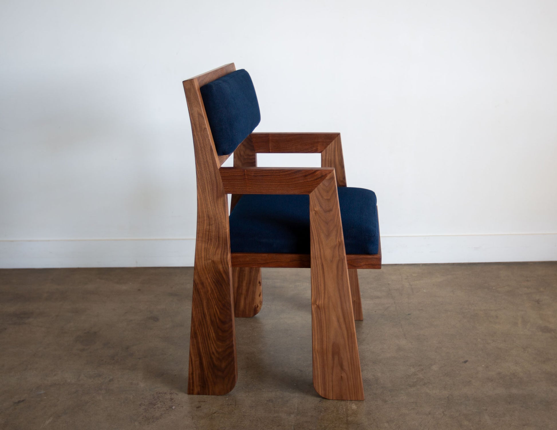 A side view of the hand-built Snyder DePass Walnut Temple Upholstered Chair, highlighting the seamless joinery of the solid walnut frame and the clean lines of the design.