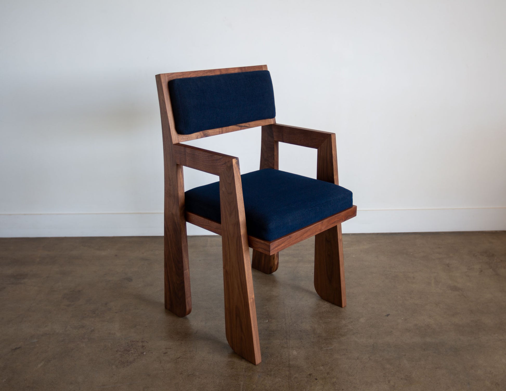 A full view of the hand-built Snyder DePass Walnut Temple Upholstered Chair, featuring a minimalist design with a rich, dark fabric and a seamless solid walnut frame.