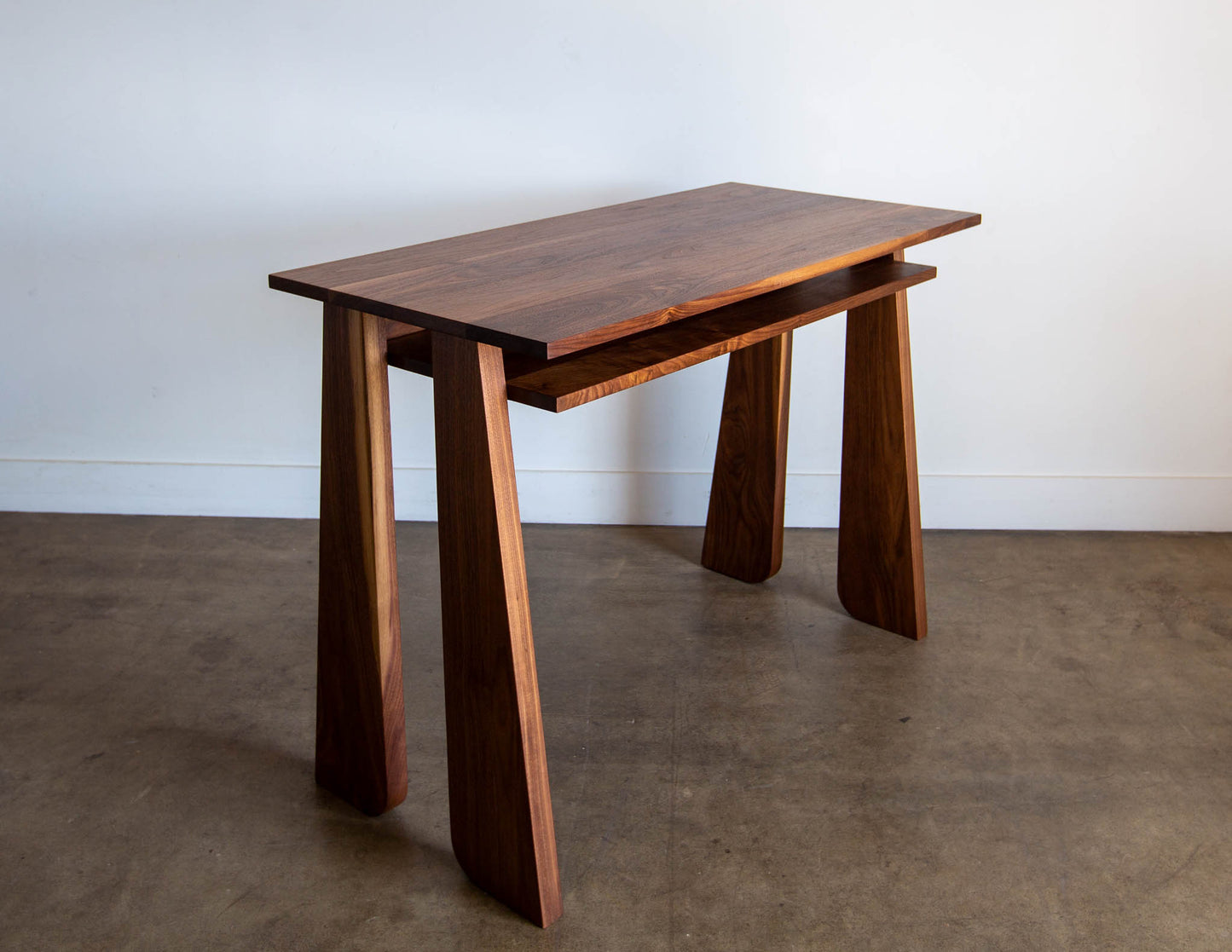 An angled view of the hand-built Snyder DePass Walnut Temple Desk, highlighting the seamless joinery and the rich grain of the solid Walnut wood. The desk's clean lines are a focal point of the modern design.