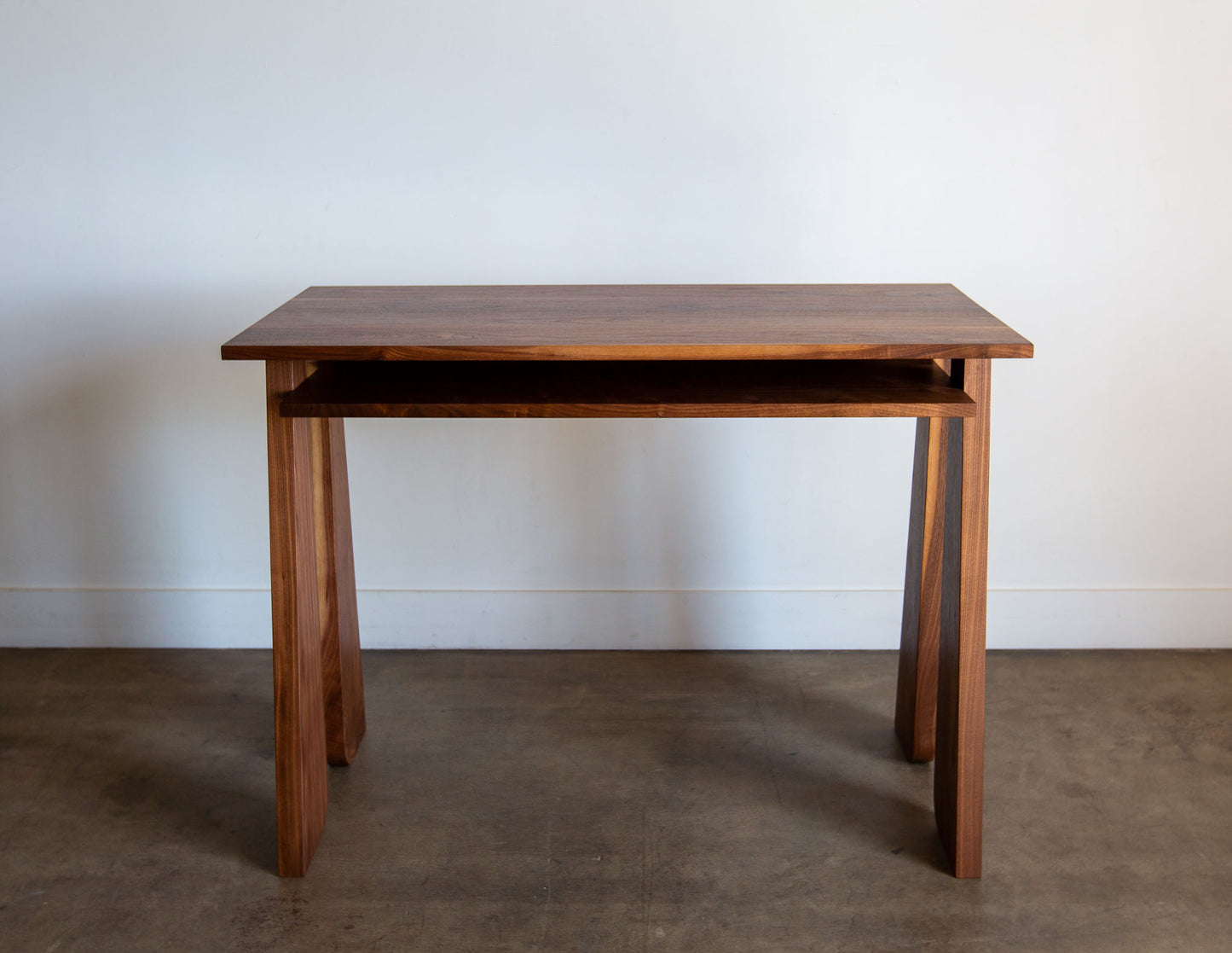 A straight-on view of the hand-built Snyder DePass Walnut Temple Desk, showing the clean, minimalist design of the tabletop and legs, and the rich grain of the solid wood.