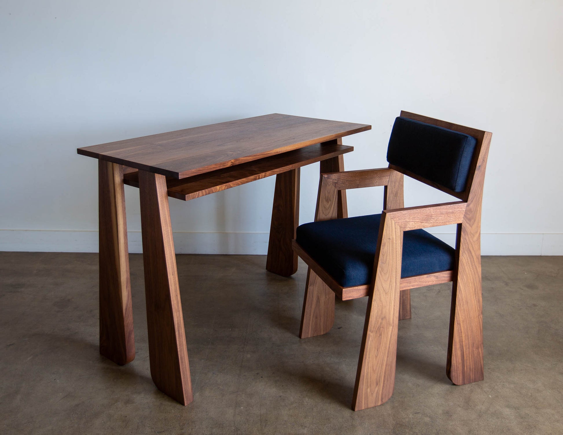 The hand-built Snyder DePass Walnut Temple Desk is shown with a matching Walnut Temple Upholstered Chair in a clean, contemporary room, highlighting its functionality and sophisticated design.