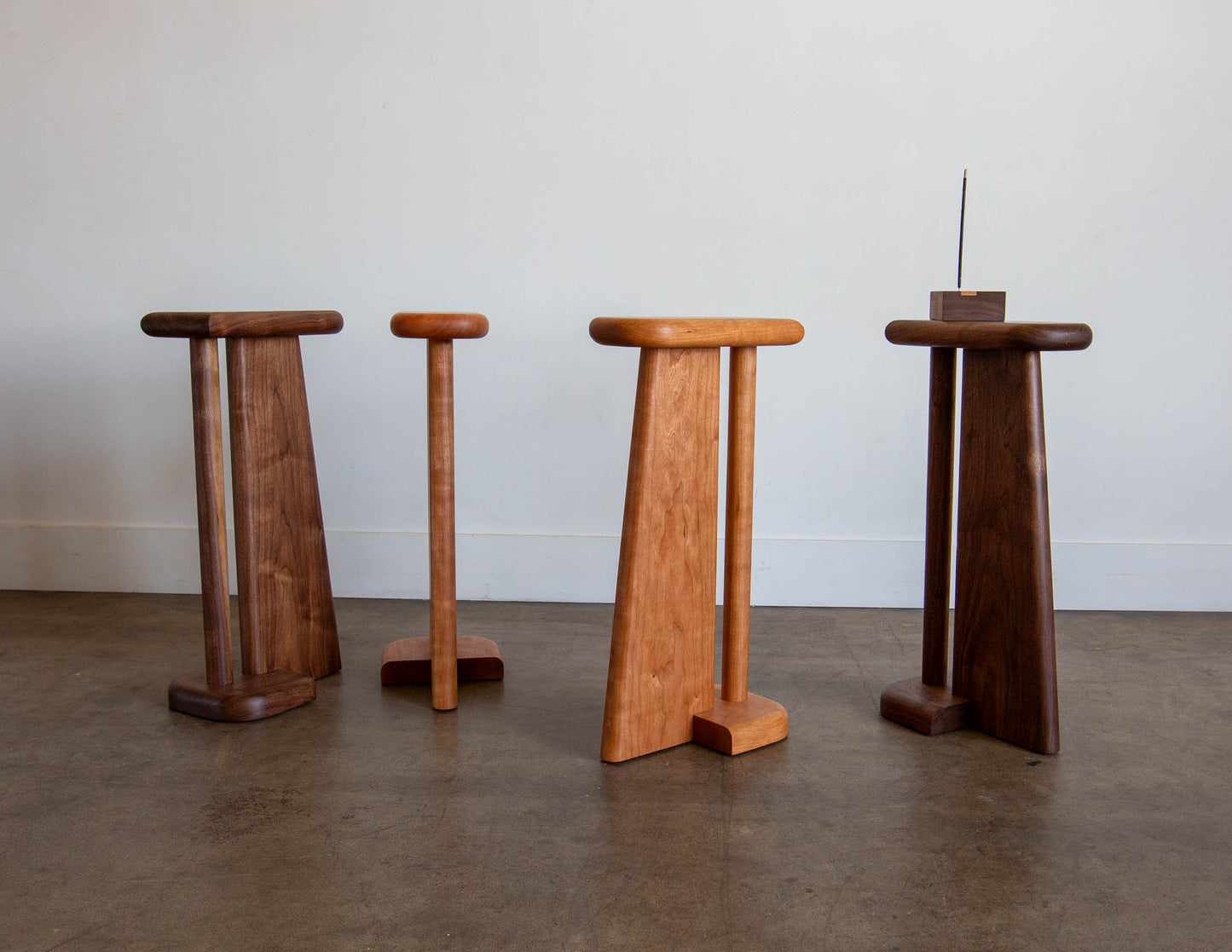 A collection of hand-built Snyder DePass Drink Stands, showcasing the different wood types (Walnut, Cherry) and their beautiful natural grain. The stands' slender and minimalist design is highlighted in a studio setting.