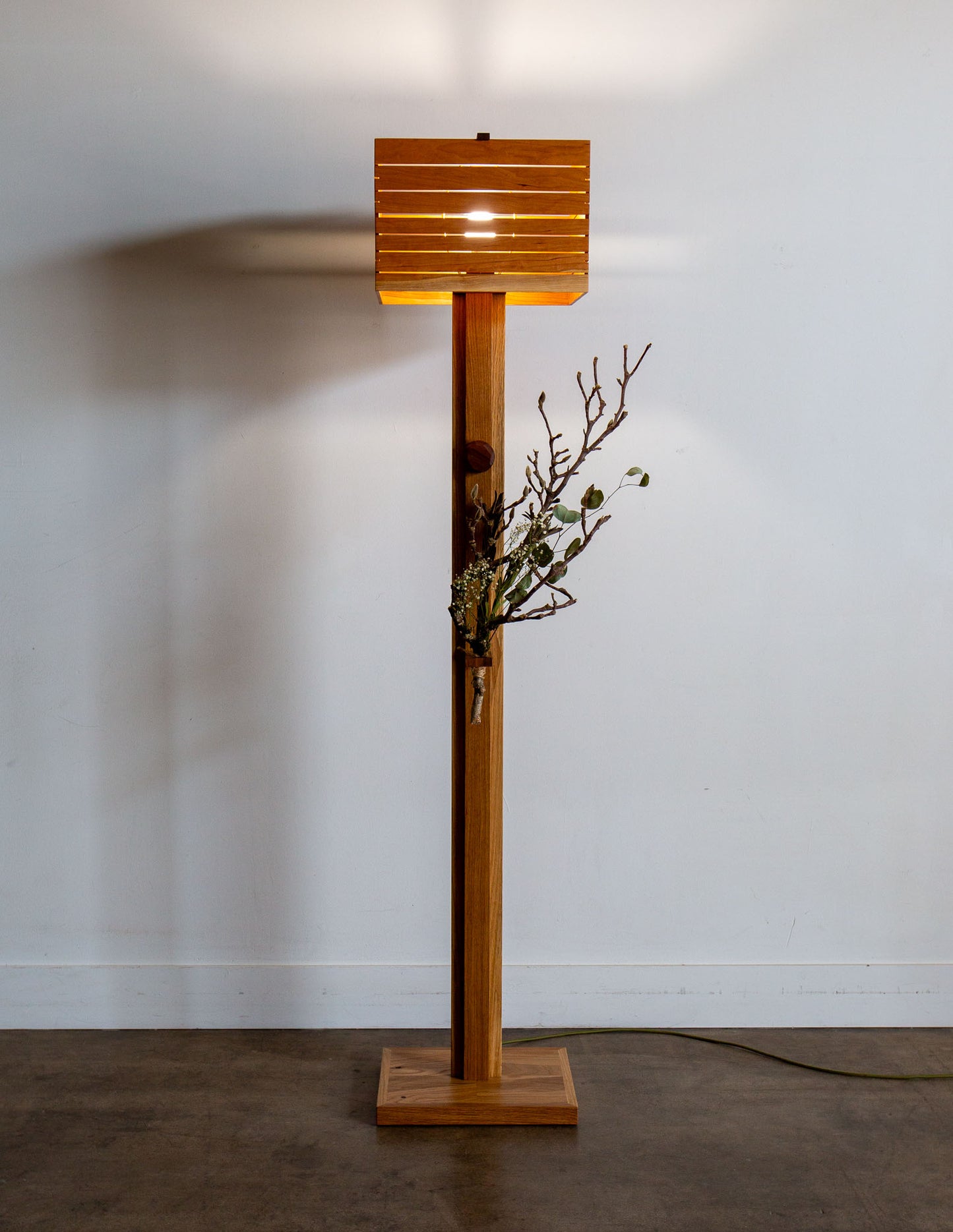 A hand-built Snyder DePass Layered Floor Lamp, featuring a unique sculptural design with multiple wooden tiers and a soft, diffused light. The lamp is a minimalist statement piece.