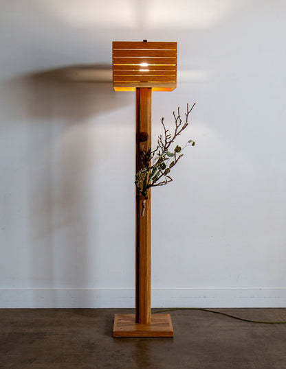 A hand-built Snyder DePass Layered Floor Lamp, featuring a unique sculptural design with multiple wooden tiers and a soft, diffused light. The lamp is a minimalist statement piece.