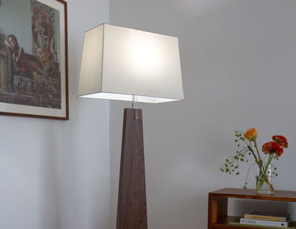 The hand-built Snyder DePass Pas Floor Lamp, with its light on, is a focal point in a modern living room, showcasing its soft, warm glow and unique sculptural design.