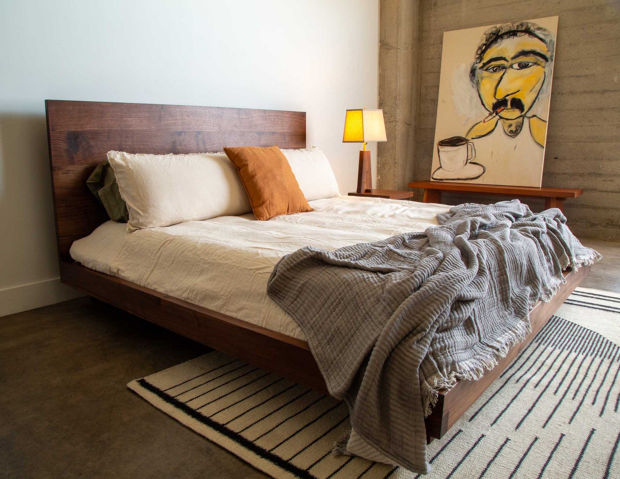 A full view of the Snyder DePass Walnut Bed, hand-built from solid Walnut, shown in a modern bedroom with clean lines and soft, neutral textiles. The bed's low profile design is a focal point of the space.