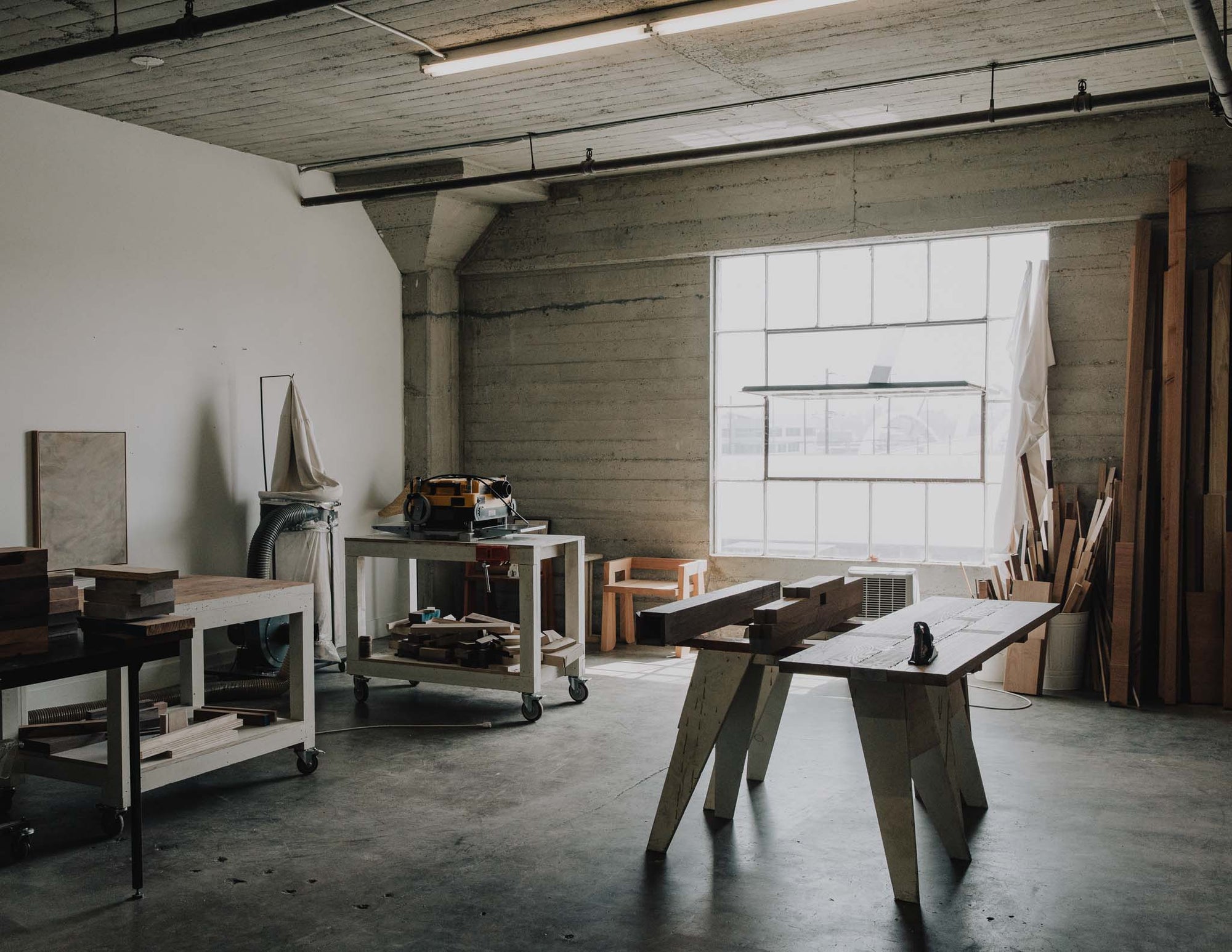 A professional photograph of the Snyder DePass studio, captured by Sean Collier, showcasing the woodworking tools, materials, and a sense of meticulous craftsmanship behind the hand-built furniture.